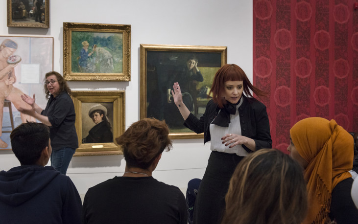 Art educator in front of audience and paintings in background