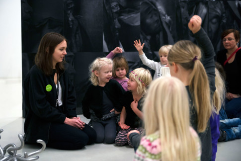 Konstpedagog sitter på golvet med en grupp barn