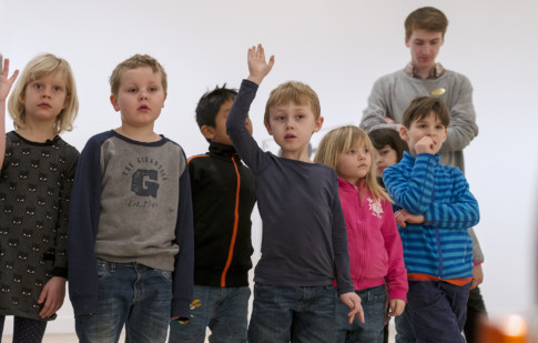 Group of children standing in exhibition hall. One child rising his hand.