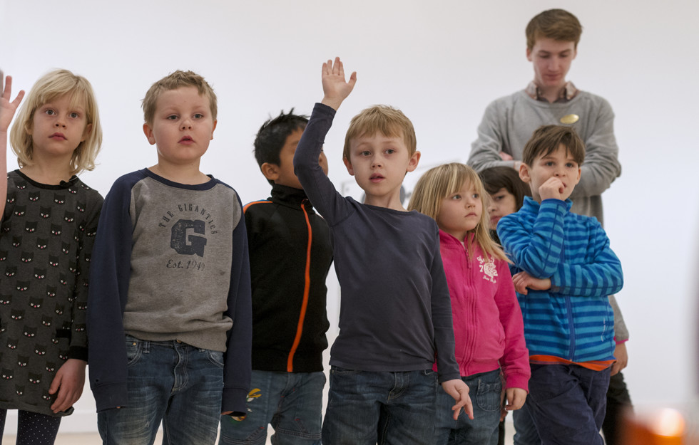 Group of children standing in exhibition hall. One child rising his hand.