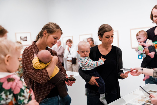 Two women carrying their babies standing in exhibition room.