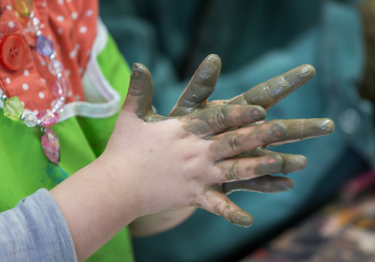 Barnhänder med lera på fingrarna.