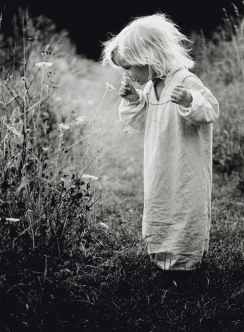 Liten flick står på äng och luktar på blomma.