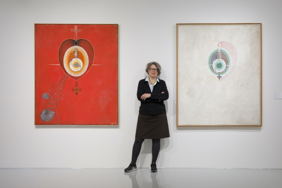 Woman standing in front of two paintings.