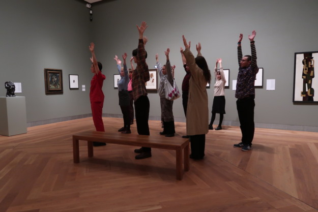 People in an exhibition room stretching up arms