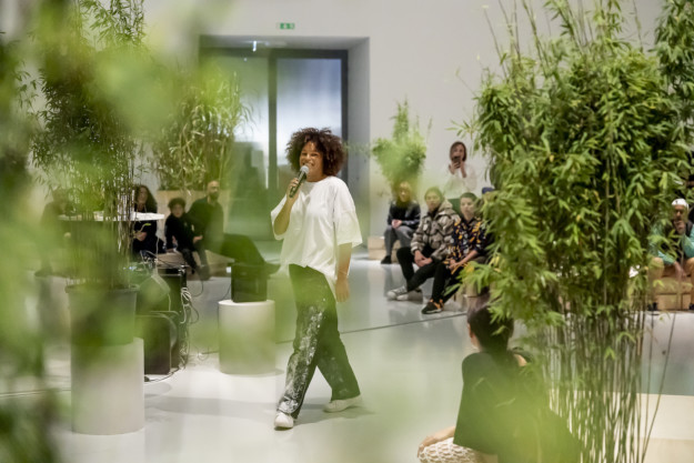 woman with microphone in room with audience and plants