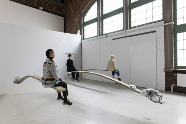 three persons sitting on planks in exhibition room