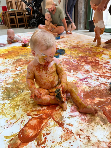 baby sitting on floor with paint all over