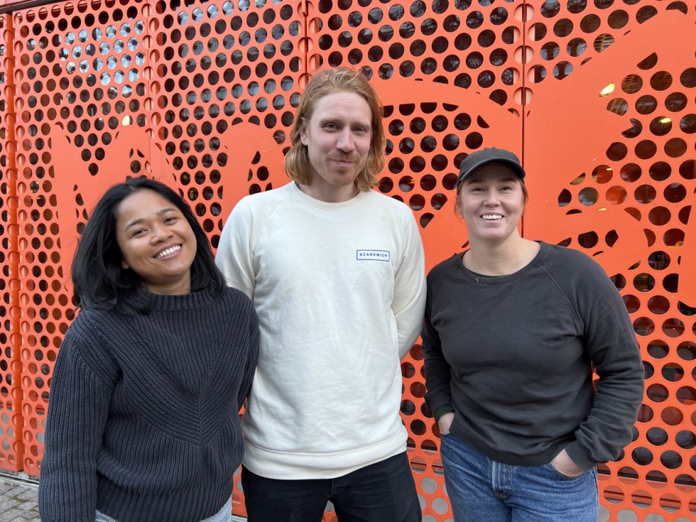 Three persons standing in front of orange building