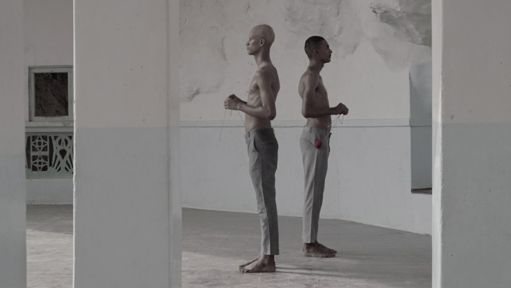 still from video with two men standing in a room