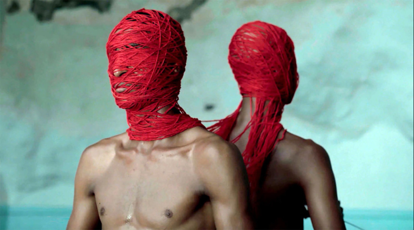 still from video with man's face covered by red yarn
