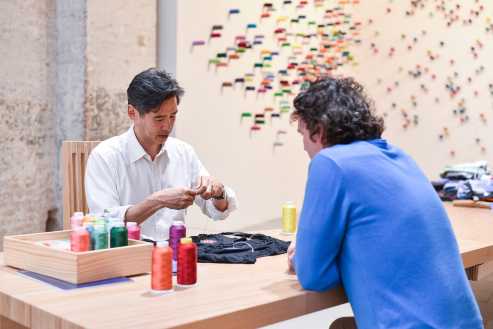 two men sitting at table sewing