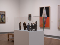 Image of a wooden scuplture group depicting black dressed persons standing around a coffin