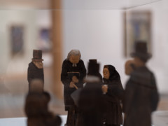 Image of a wooden scuplture group depicting black dressed persons standing around a coffin