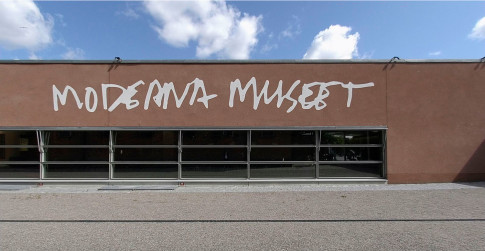 Modern Museum's facade with logo painted on brown stone wall.
