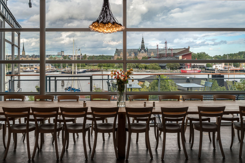 Chairs at a long table in front of a large window overlooking water.