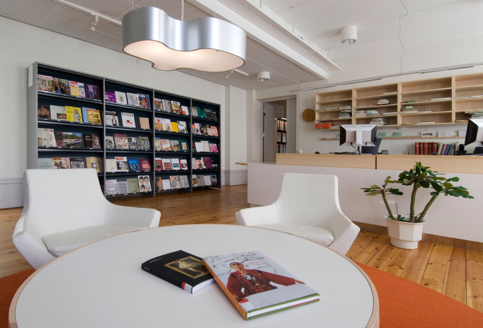 Low table with armchairs in front of bookshelf and library counter in a bright room.