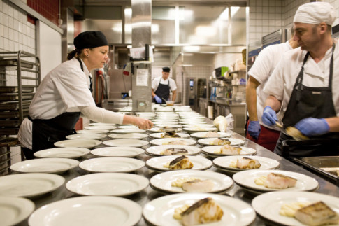Rows of plates and staff working in restaurant kitchen.