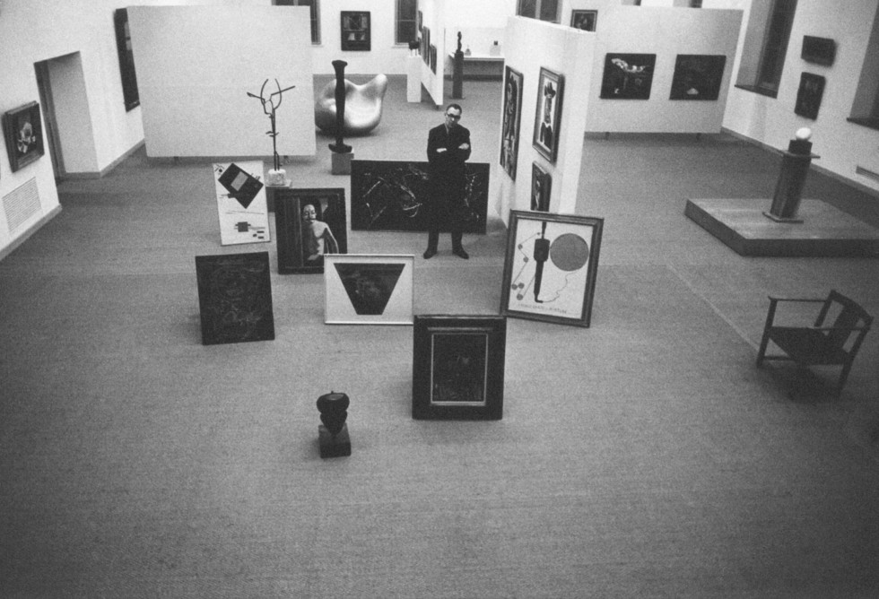 Man som står i utställningssal omgiven av konstverk.
