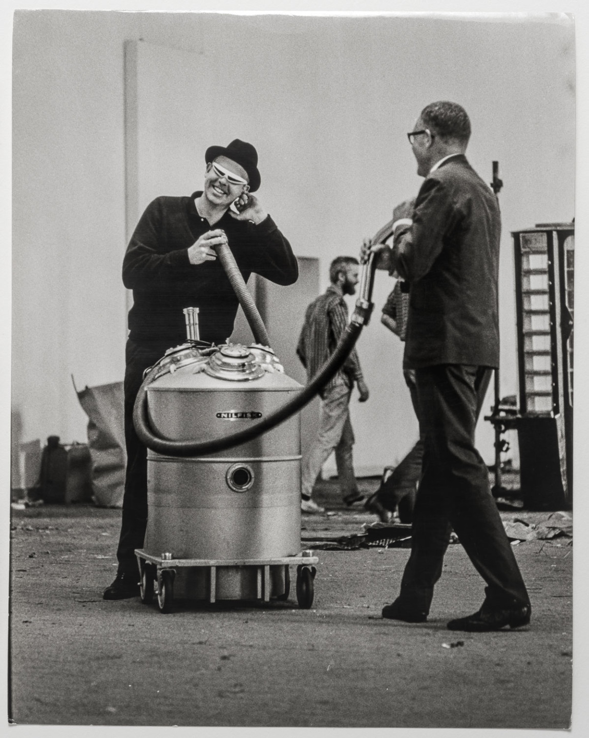 Svartvitt fotografi av Pontus Hultén och Claes Oldenburg som håller i två slangar från en stor damsugare.