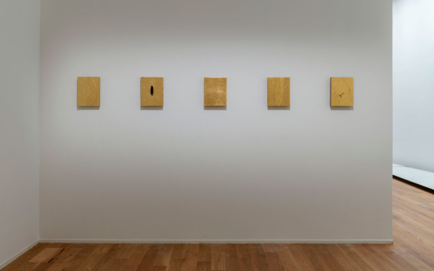 Gold colored, square shaped artworks on white wall.