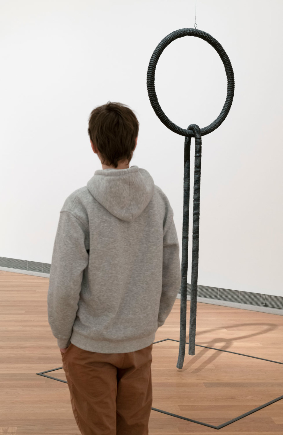 Person standing in front of the artwork Untitled by Eva Hesse: Painted rope wrapped around plastic hose and ring in wood and metal