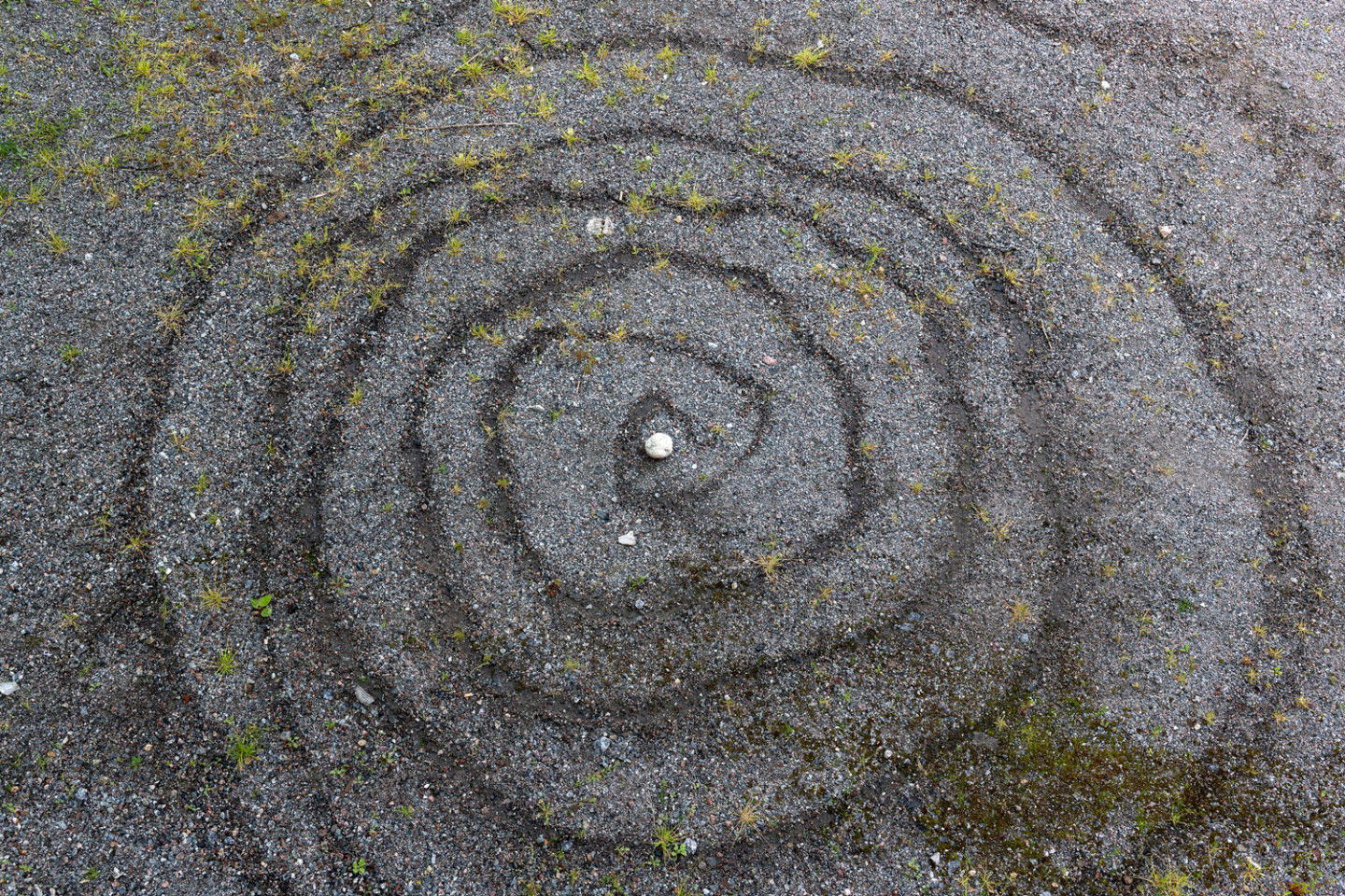 Spiral of water on gravel with a white stone in the middle.