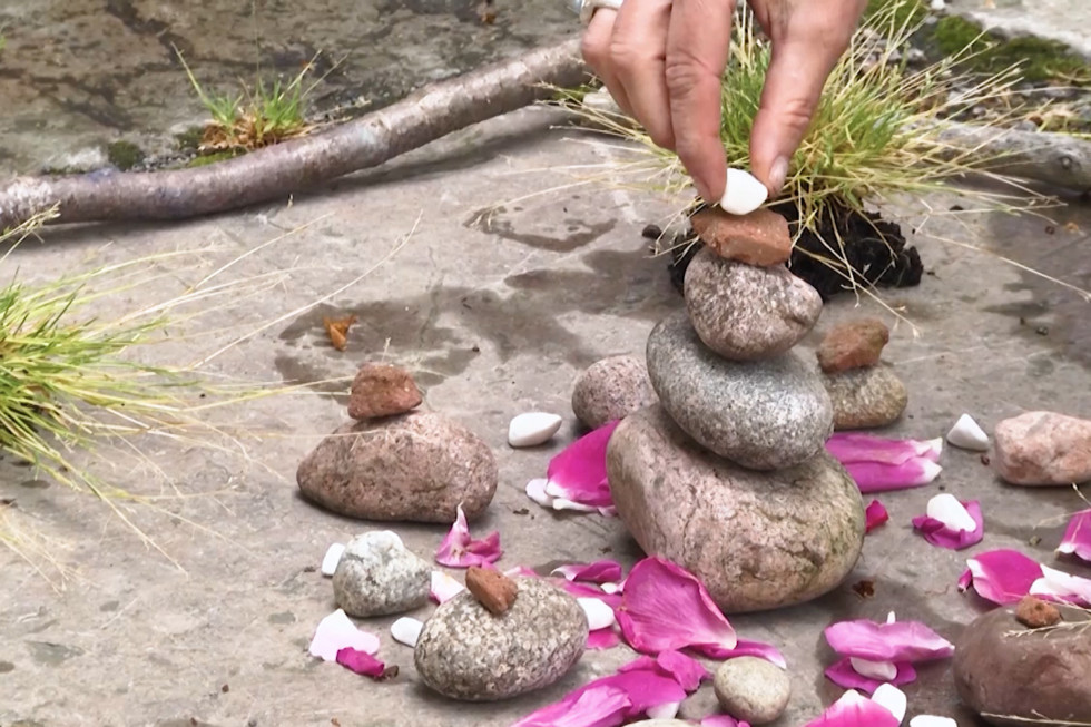 Hand places a small white stone on top of some gray stones stacked on each other.