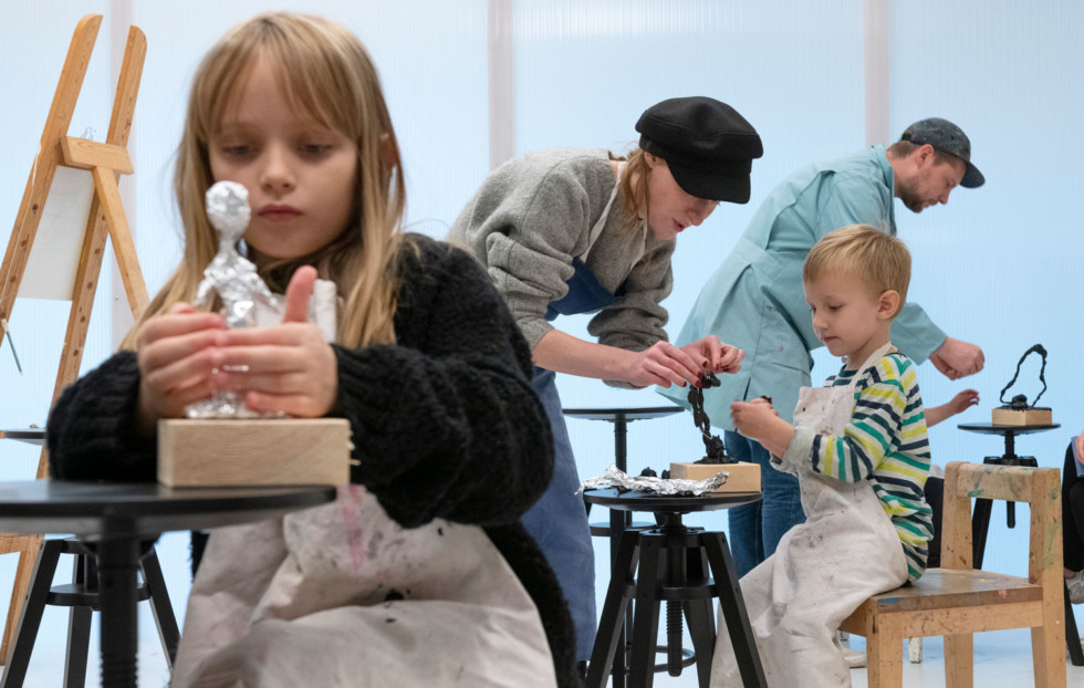 Barn sitter på stolar i verkstan och gör skulpturer i folie och lera