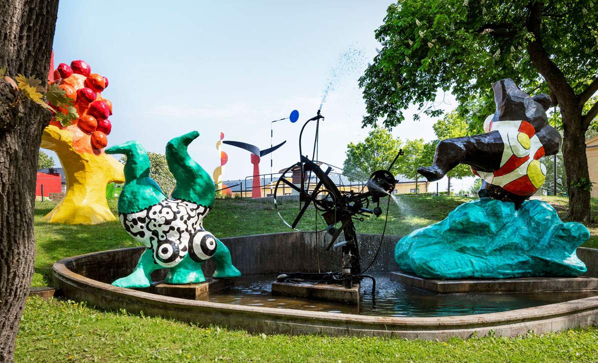 Colorful sculptures on lawn and lush trees.