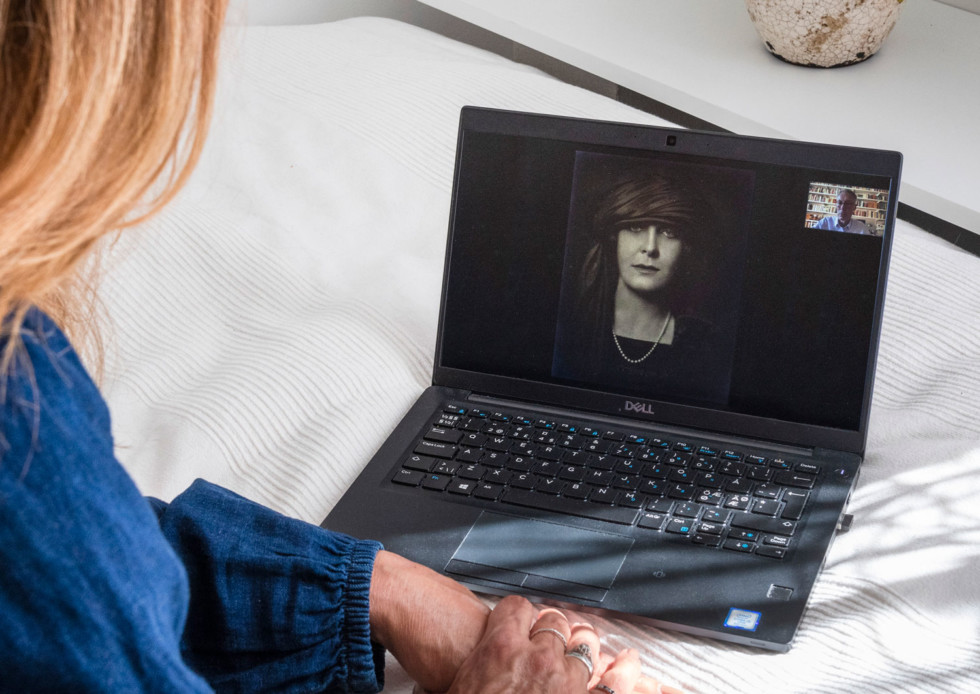 Person sitter framför en datorskärm som visar ett svartvitt fotografi och en person som pratar.