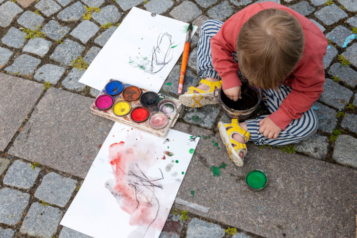Child sitting on the ground painting with watercolors.
