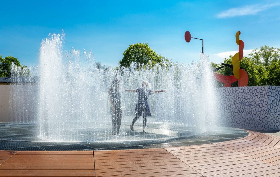 Två personer rör sig i Jeppe Heins stora fontän på Exercisplan utanför museet