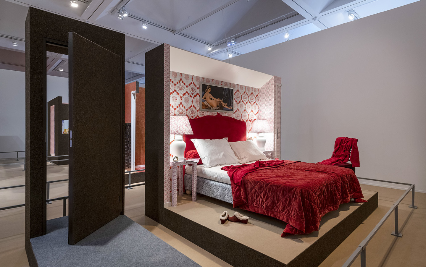 A double bed with red bedspread, bedside lamps and small tables on both sides.