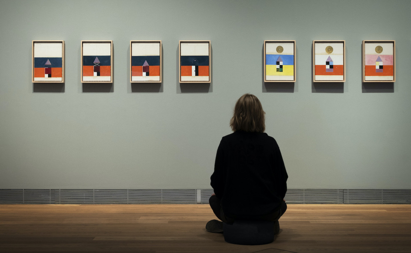 Photo of person sitting in front of a row with small paintings