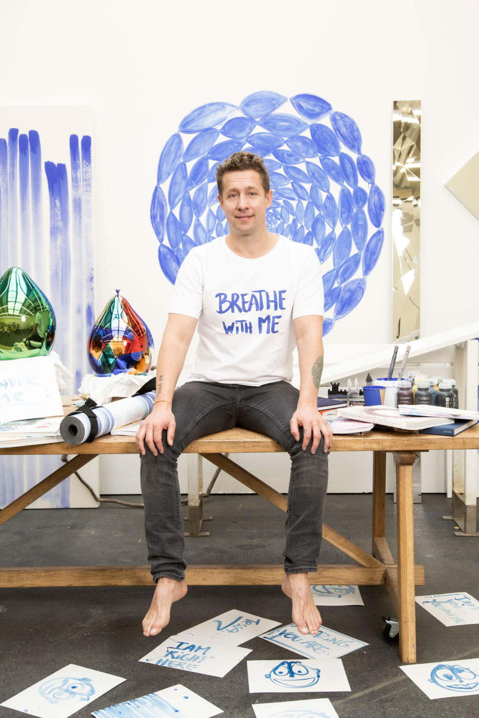 Konstnären Jeppe Hein sitter på ett skrivbord, på golvet ligger papper utspridda