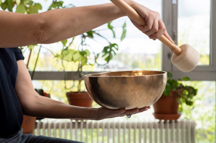 En person slår med en trästav på en så kallad "Singing bowl" - klangskål