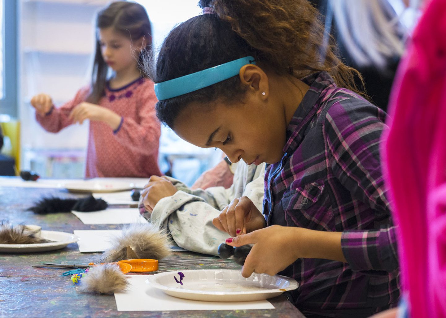 A child is sittting down at a table, focused on creating with clay