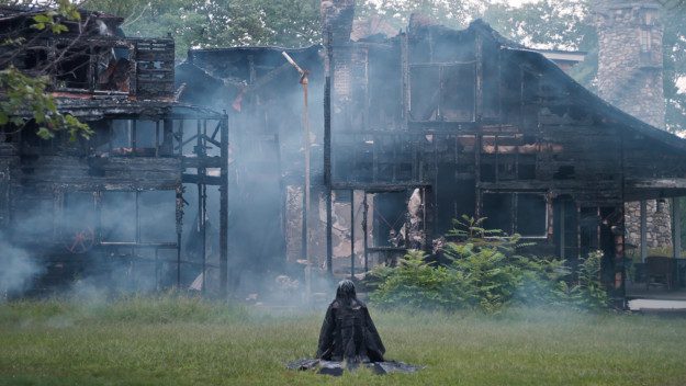 A figure in front of a burned out house