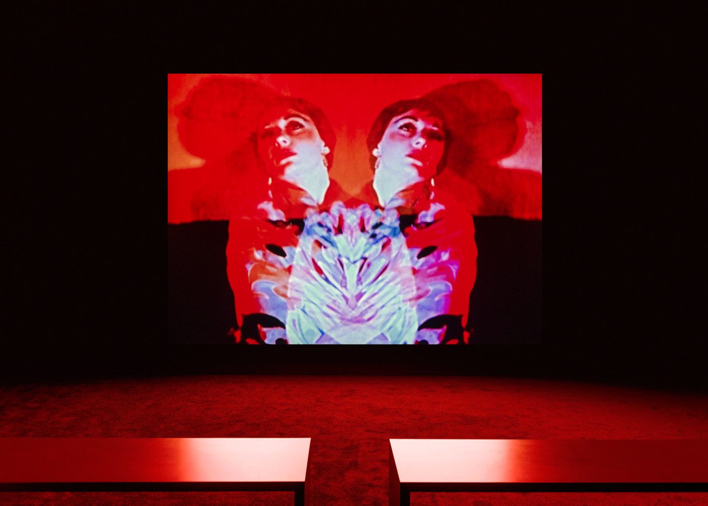 Color image projected on the wall, two benches in the foreground of the room