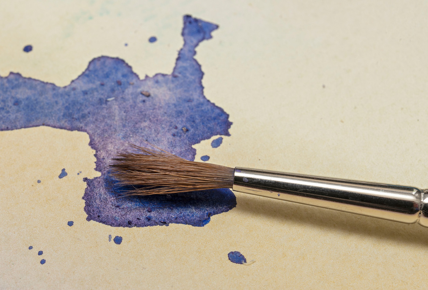 Closeup of a watercolor brush, a stroke of blue watercolor on a white paper.