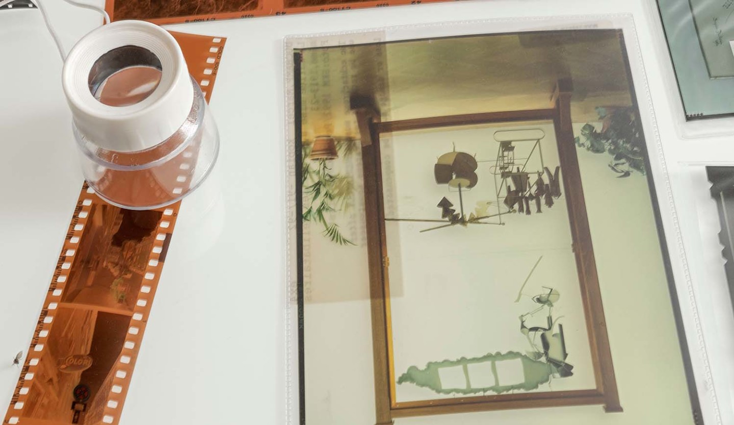 A magnifying glass is placed on top of a film strip. Also included in the image is a developed photograph of Marcel Duchamp's artwork "The Bride Stripped Bare by Her Bachelors, Even".