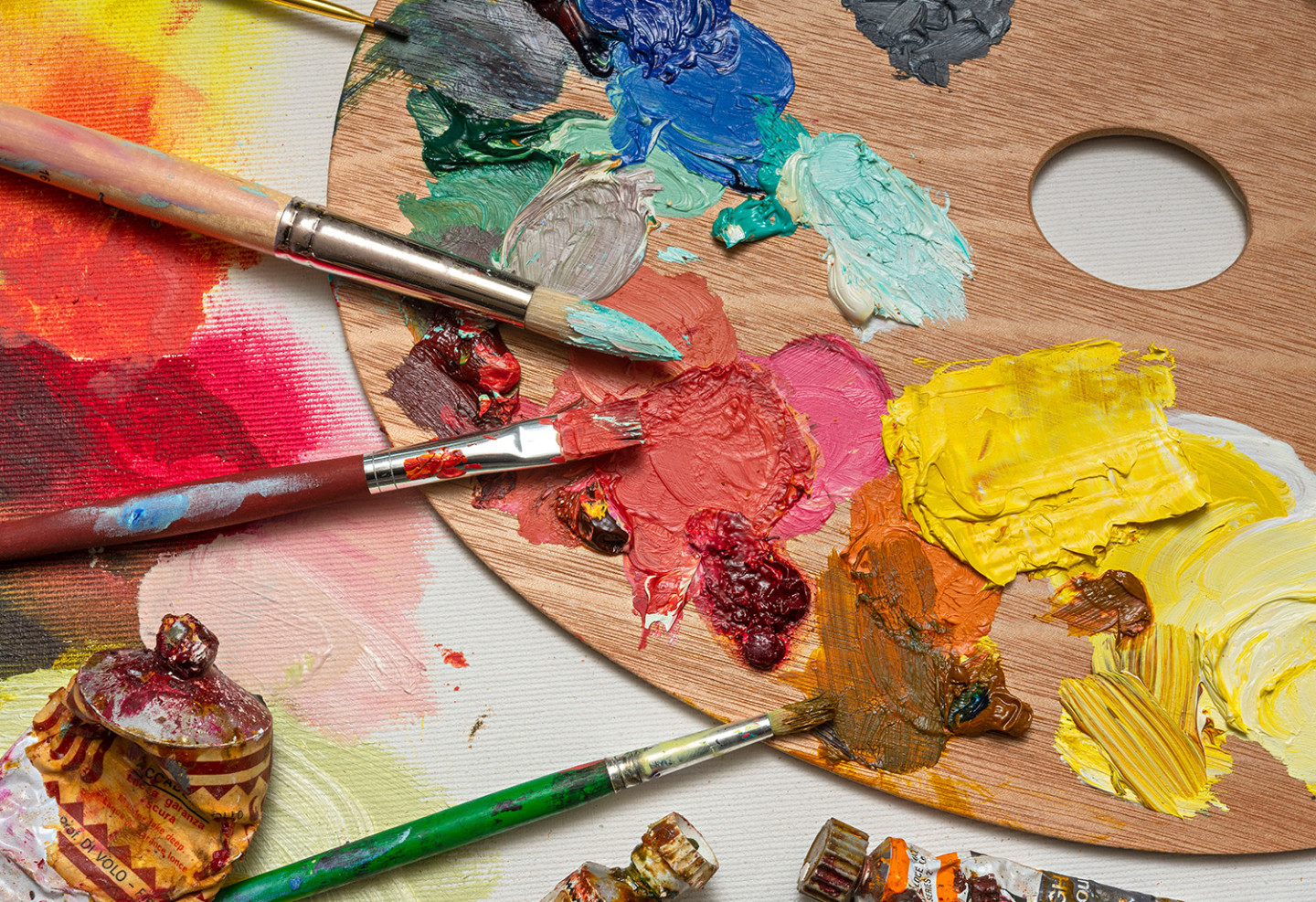 Palett med oljefärger i blått, rosa och gult. Penslar som har använts för att måla med färgerna ligger på paletten. 
