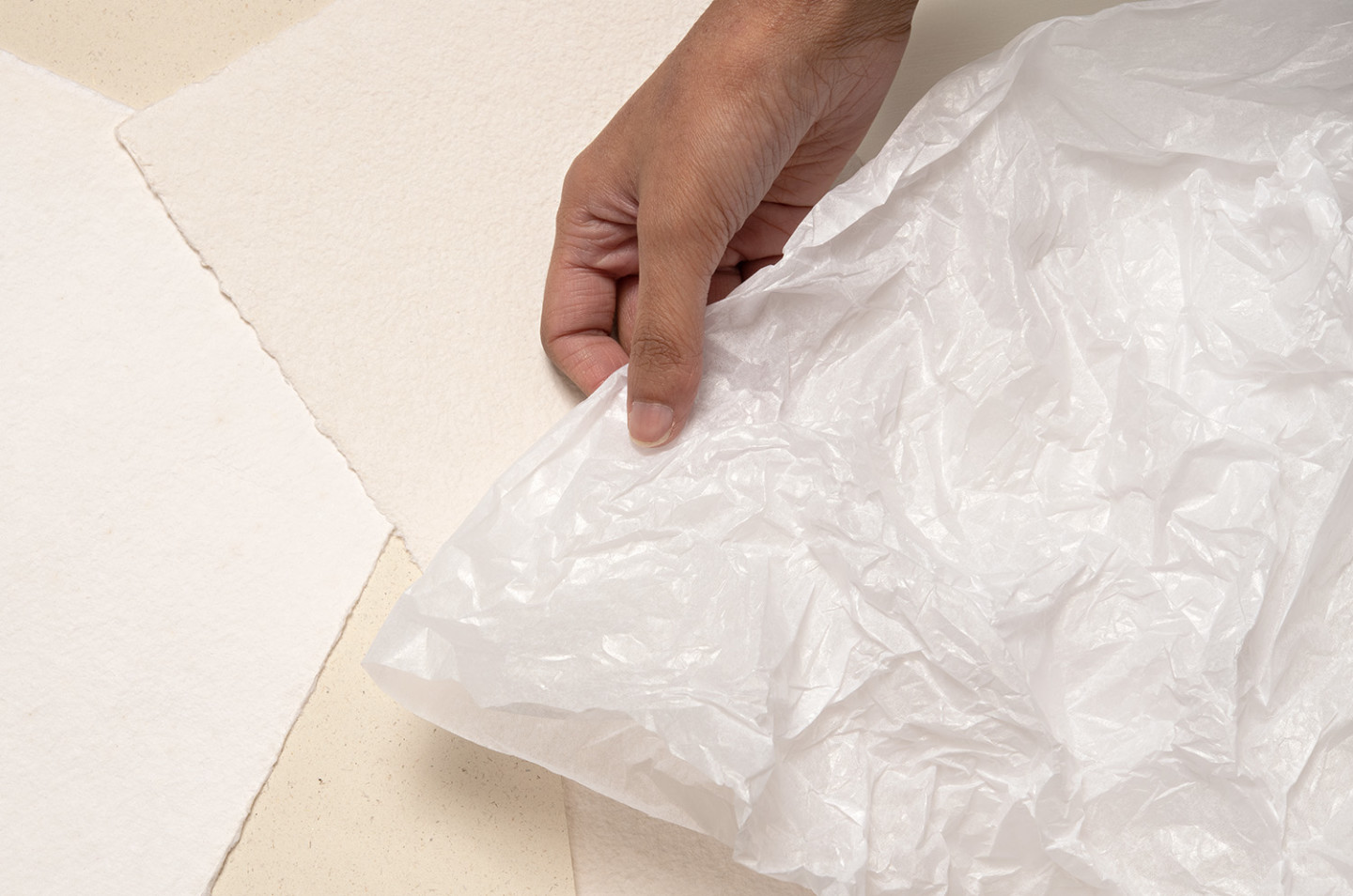 A hand holds a white sheet of tissue paper.