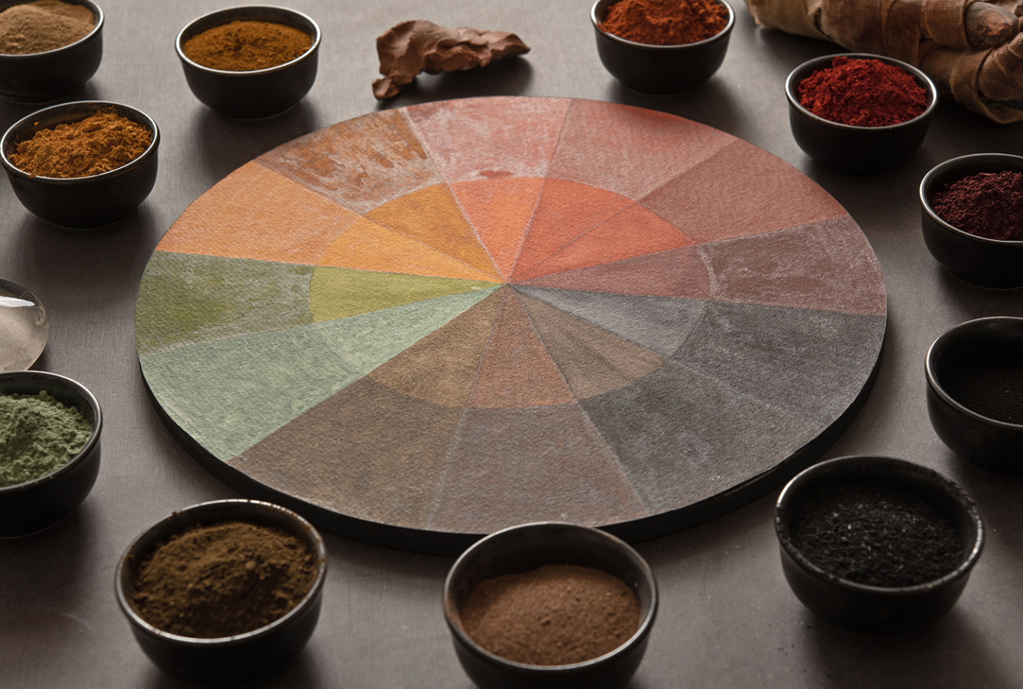 Bowls with pigments in different colors are arranged around a wooden color circle.