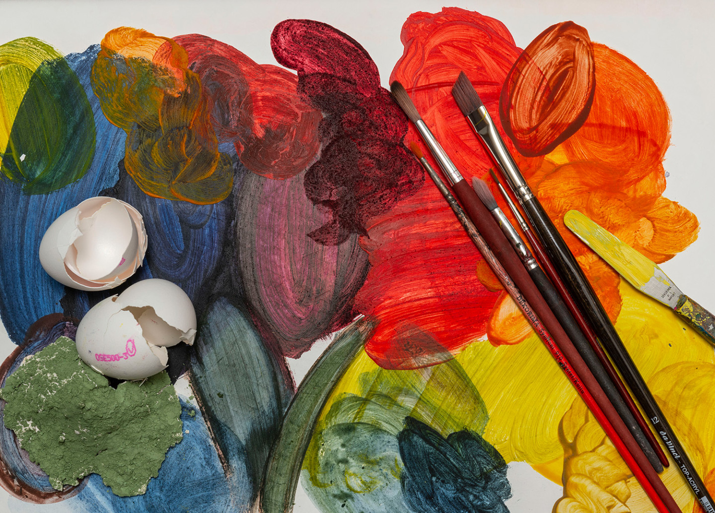 Tempera painting, different colors: green, yellow, red. Paintbrushes and a cracked egg.