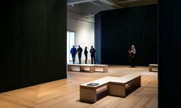 A group of people stand between the exhibition rooms in "Nan Goldin – This Will Not End Well"