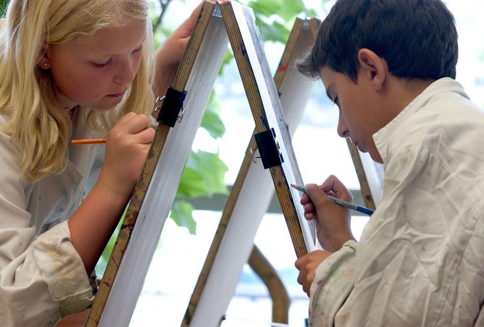 Två barn målar på varsitt staffli.