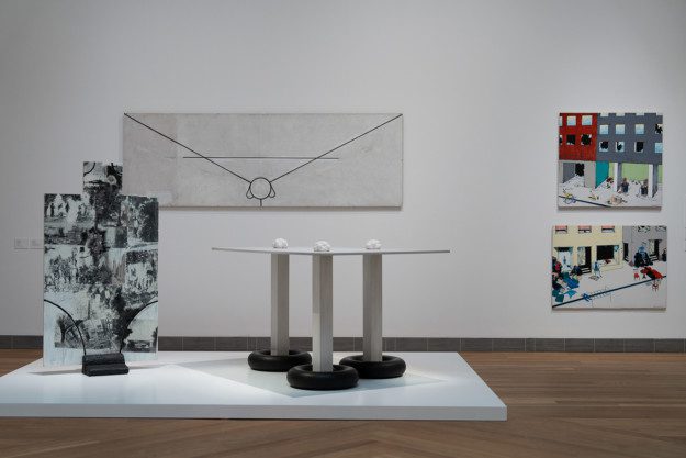 Installation view over the exhibition. Sculptures are placed on a white podium, with two artworks hanging on a white wall in the background.