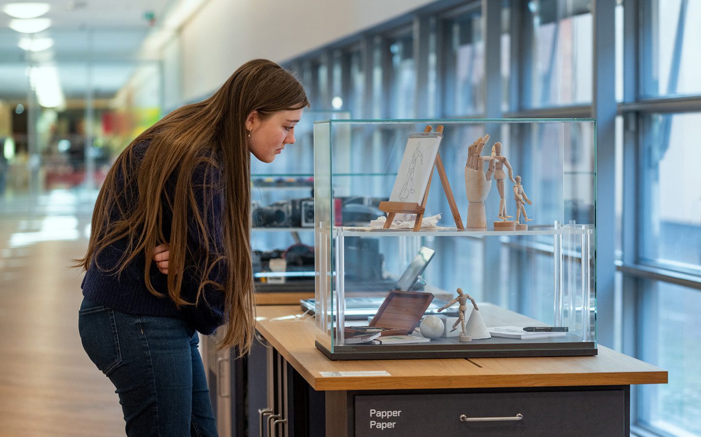 En flicka tittar på redskap för skissning genom en glasmonter i utställningen "Konstens byggstenar"
